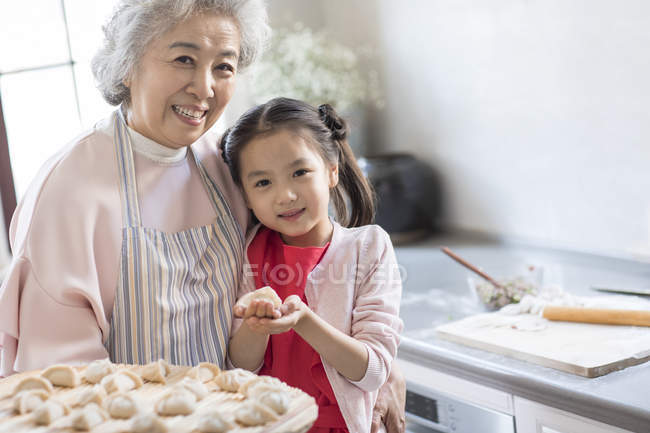 Chinese granddaughter and grandmother making dumplings in kitchen — Stock Photo