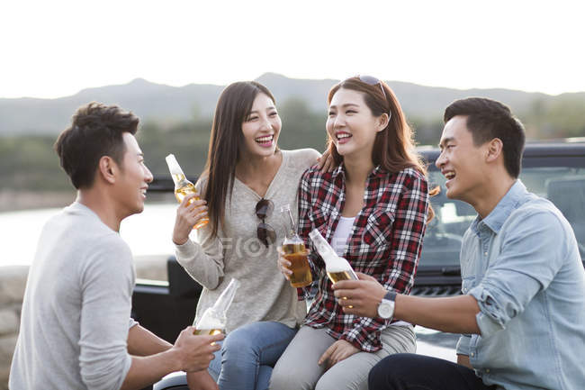 Chinese friends sitting with beer on car — Stock Photo
