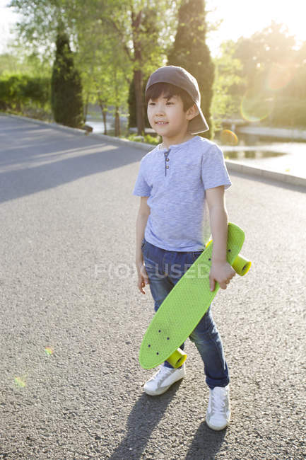 Китайский мальчик позирует со скейтбордом на дороге — стоковое фото