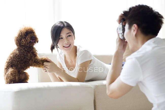 Chinese man taking photos of woman and pet poodle at home — Stock Photo