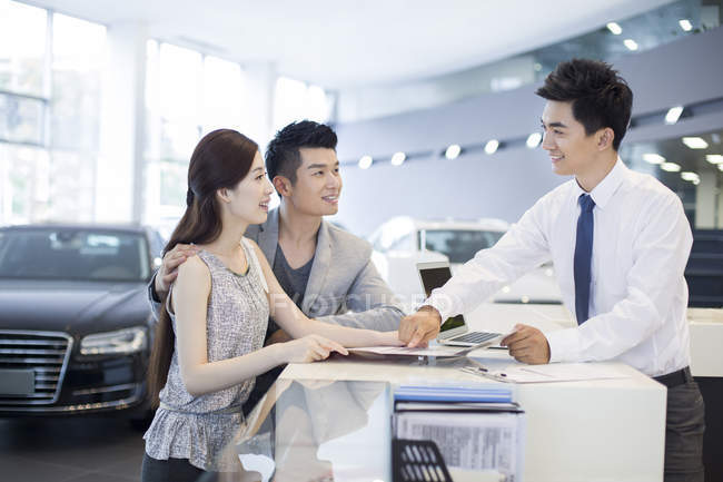 Casal chinês conversando com revendedor ao escolher o carro no showroom — Fotografia de Stock