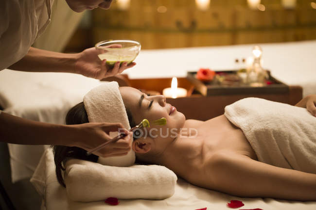 Young Chinese woman having facial mask treatment in spa center — Stock Photo