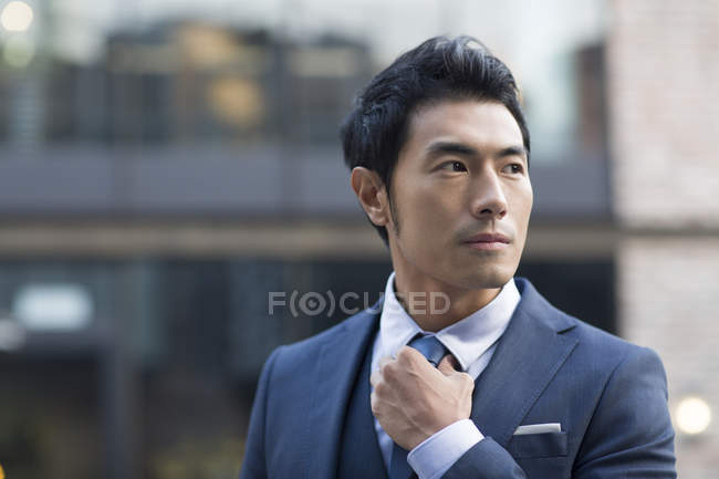 Азиатский мужчина выпрямляет галстук на улице — стоковое фото