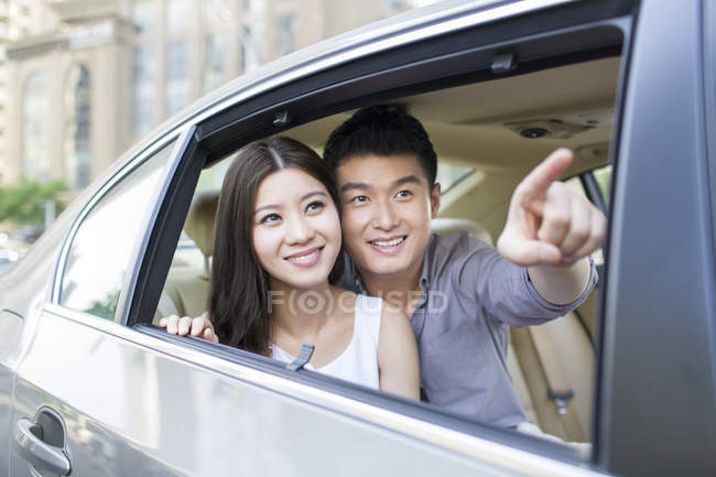 Chinese couple on car back seat pointing in window — Stock Photo