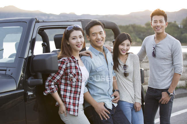Chinese friends posing with car in suburbs — Stock Photo