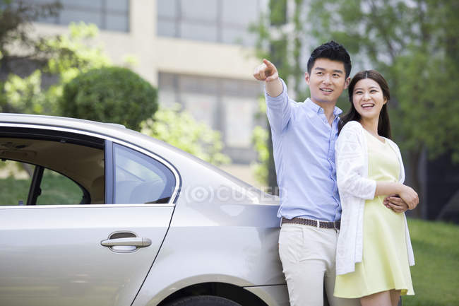 Chinese couple pointing and leaning on car — Stock Photo