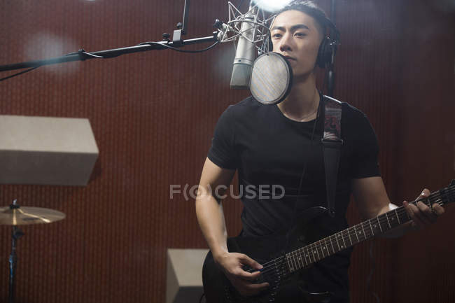 Chinese man singing with guitar in recording studio — Stock Photo