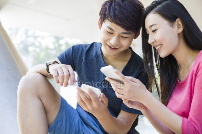 Couple chinois regardant les smartphones et souriant dans la rue — Photo de stock