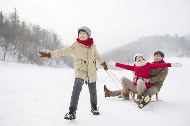 Китайский мальчик тянет сани с родителями на снегу — стоковое фото