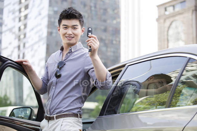 Chinese man posing with keys in front of car — Stock Photo