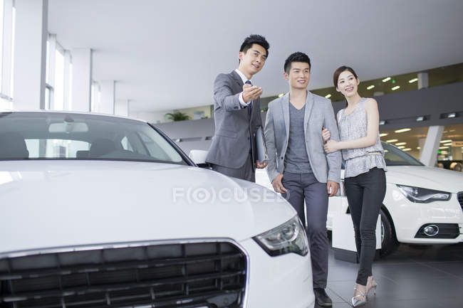 Revendeur de voitures montrant des voitures au couple chinois dans la salle d'exposition — Photo de stock