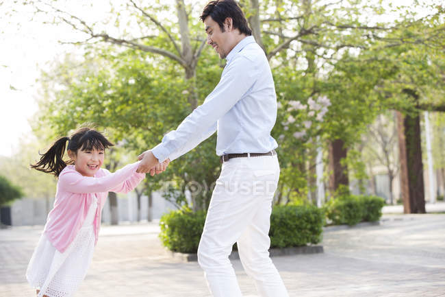 Asian father and daughter spinning around in park — Stock Photo