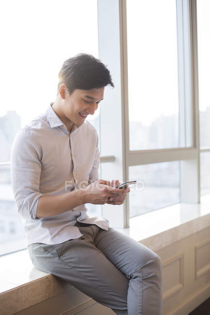 Young man using smartphone on window sill — Stock Photo