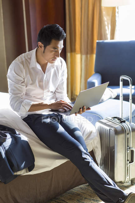 Homme d'affaires chinois utilisant un ordinateur portable sur le lit dans la chambre d'hôtel — Photo de stock