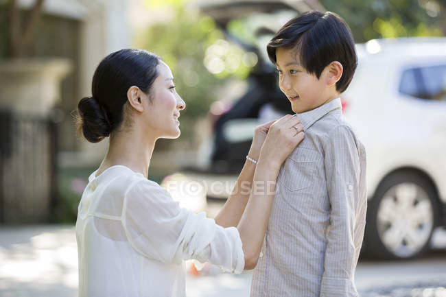 Chinese mother buttoning son shirt on street — Stock Photo