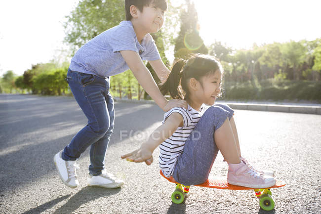 Chinese boy pushing girl on skateboard — Stock Photo