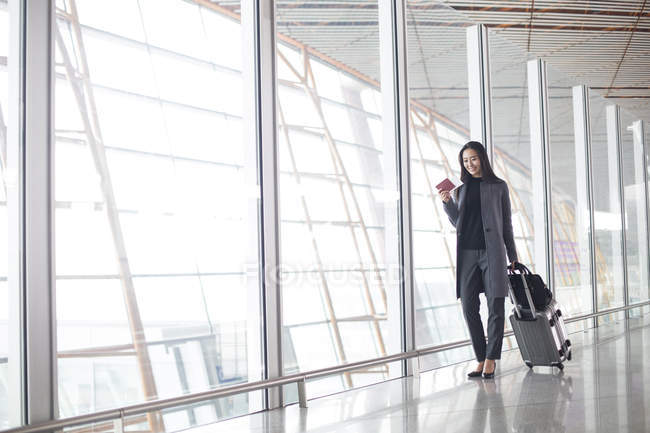 Asian woman pulling luggage in airport lobby — Stock Photo