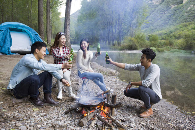 Chinese friends sitting around campfire with beer — Stock Photo