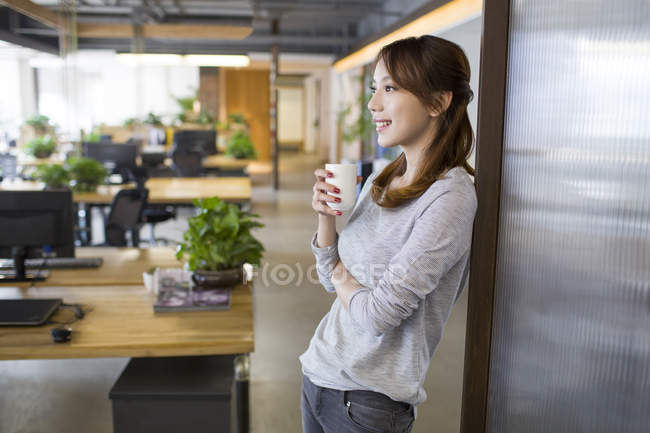 Chinese woman drinking coffee in office — Stock Photo