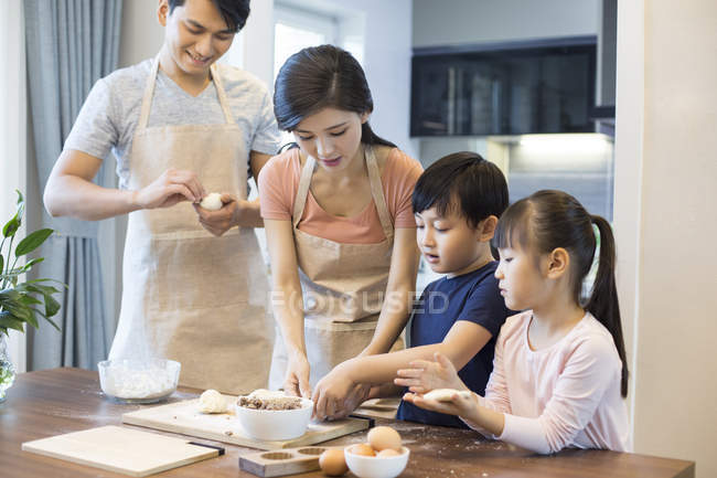 Familia china con hermanos horneando juntos en la cocina - foto de stock