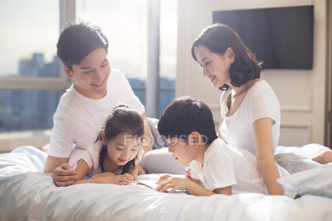 Pais chineses e crianças lendo livro na cama — Fotografia de Stock