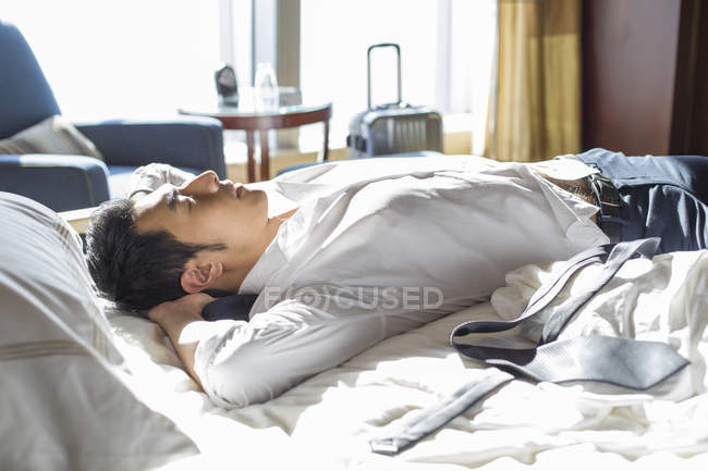 Hombre de negocios chino descansando en la cama en la habitación de hotel - foto de stock