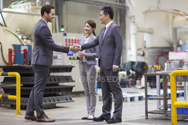 Empresarios estrechando manos en fábrica industrial - foto de stock