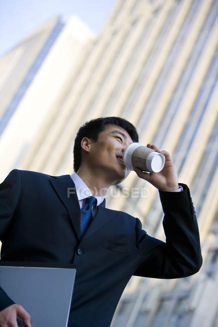 Chinese man drinking coffee and holding documents on street — Stock Photo