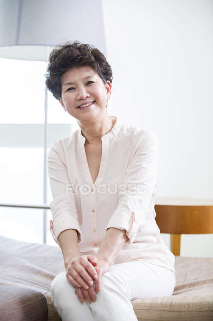 Senior Chinese woman sitting in sofa and looking in camera — Stock Photo