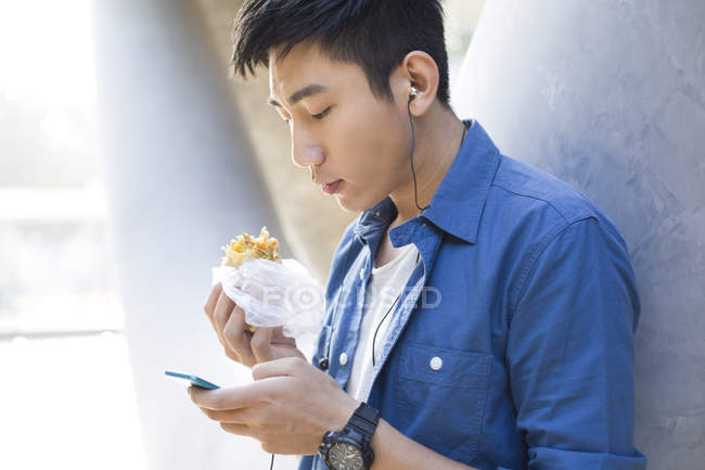 Hombre chino comiendo comida y usando teléfono inteligente - foto de stock