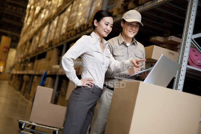 Chinese businesswoman in warehouse with workers using laptop — Stock Photo