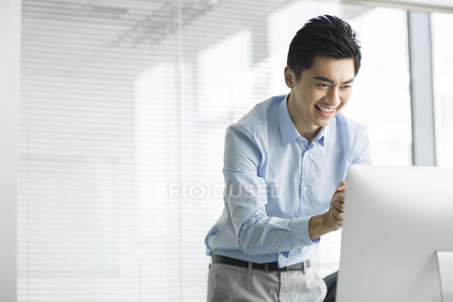 Hombre de negocios chino sonriendo y utilizando la computadora en la oficina - foto de stock