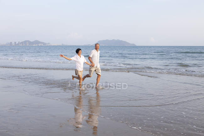 Старшая китайская пара бегает по пляжу — стоковое фото