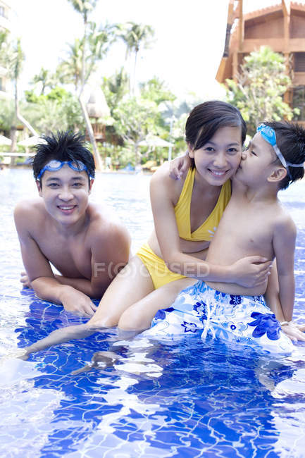 Padres chinos con hijo divirtiéndose y posando en piscina - foto de stock