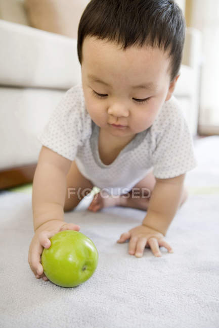 Китайский мальчик ползает и играет с зеленым яблоком на ковре — стоковое фото