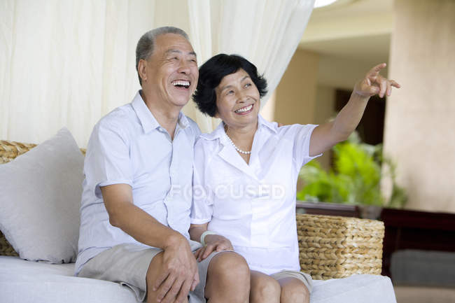 Старшая китайская пара сидит на диване на курорте и указывает — стоковое фото