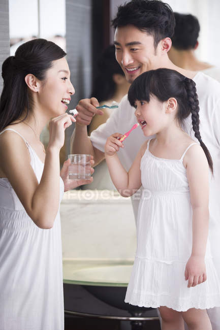 Padres chinos con hija cepillándose los dientes en el baño - foto de stock