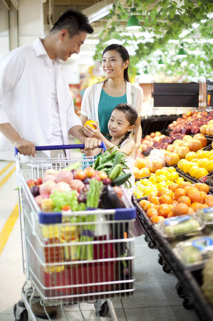 Chinese girl with parents buying fruits in supermarket — Stock Photo