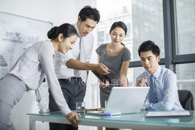 Gli uomini d'affari cinesi che parlano e guardano il computer portatile in riunione — Foto stock