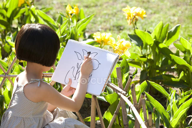 Маленькая девочка рисует желтые цветы в саду — стоковое фото