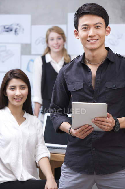 Designer cinese in possesso di tablet digitale con il team in background — Foto stock