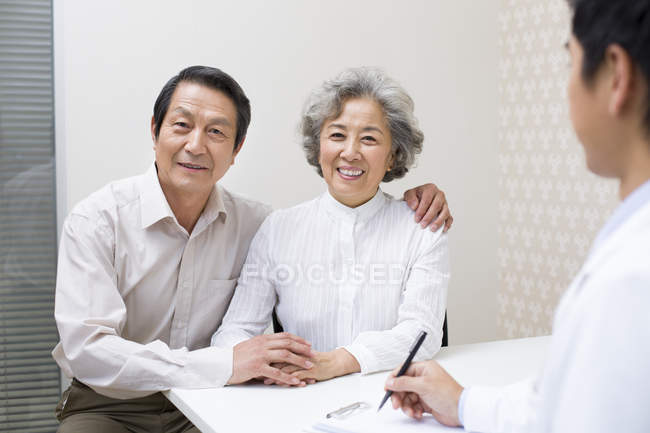 Casal sênior chinês sentado com médico no hospital — Fotografia de Stock