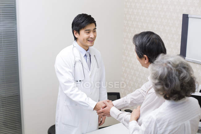 Casal sênior chinês apertando as mãos com o médico no hospital — Fotografia de Stock