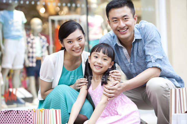 Chinois parents et fille posant avec des sacs à provisions dans le centre commercial — Photo de stock