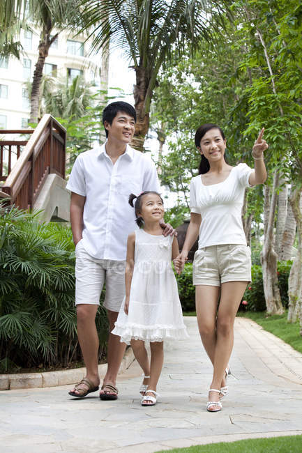 Padres chinos con hija caminando y señalando el complejo turístico - foto de stock