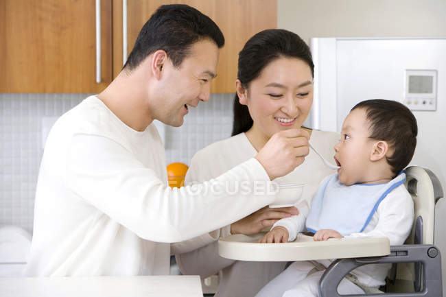 Chinese parents feeding baby boy in high chair — Stock Photo