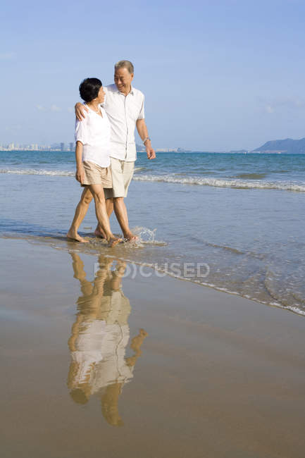 Старшая китайская пара прогуливаясь вдоль морского пляжа — стоковое фото