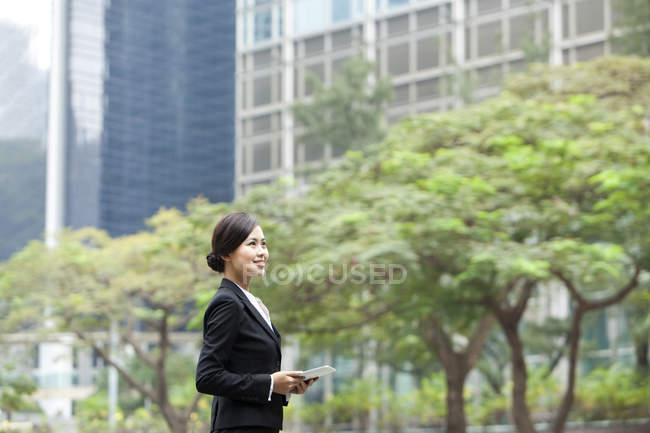 Donna d'affari cinese guardando con tablet digitale in mano sulla strada — Foto stock