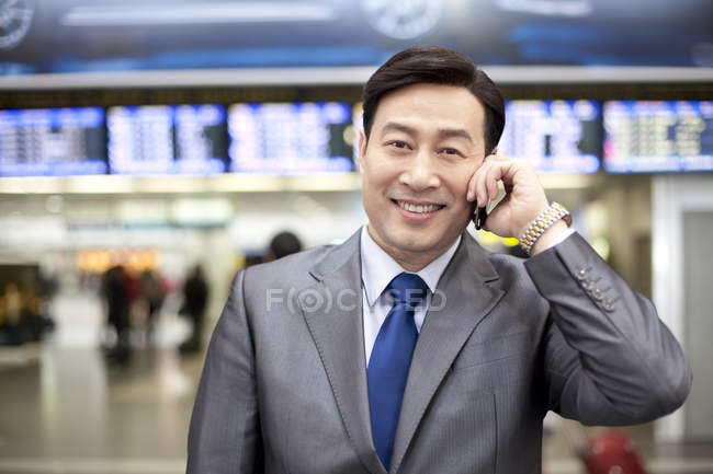 Chinese businessman talking on phone at airport — Stock Photo