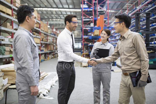 Businessman shaking hands with engineer in factory — Stock Photo